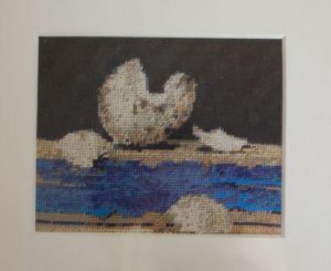 Minibillede af kunstkort broderet med petit point. æggeskaller på blå hylde.